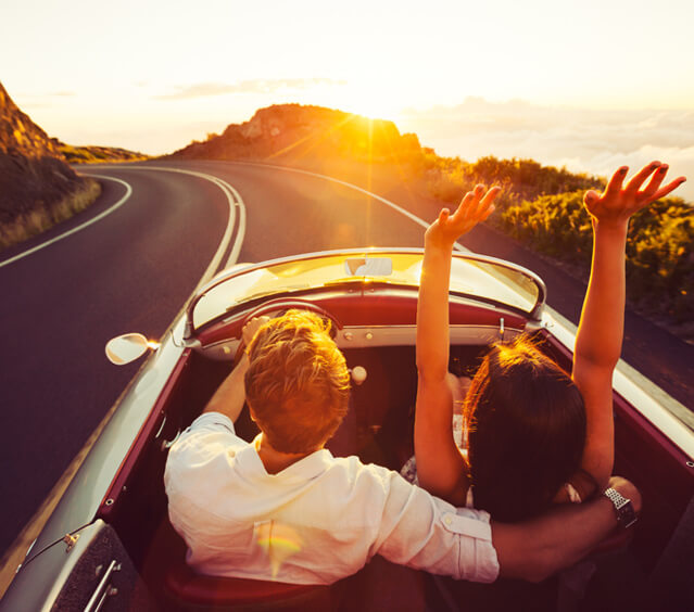 Pärchen im Elektroauto fährt in den Sonnenuntergang Pärchen im Elektroauto fährt in den Sonnenuntergang