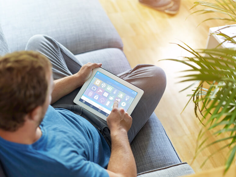 Mann auf der Couch bedient Smart Home über sein Tablet Mann auf der Couch bedient Smart Home über sein Tablet